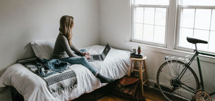 This image shows someone sitting on a bed with a laptop open.